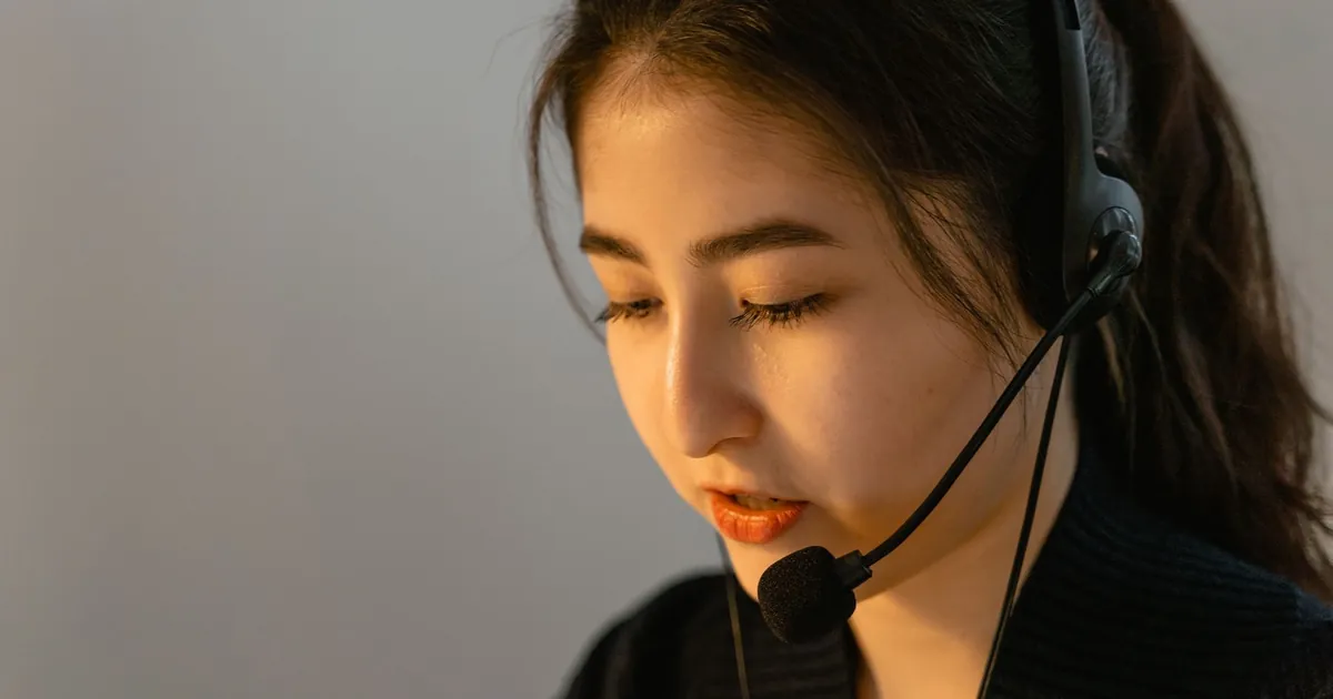 Focused young woman in headset working in customer support, speaking attentively.