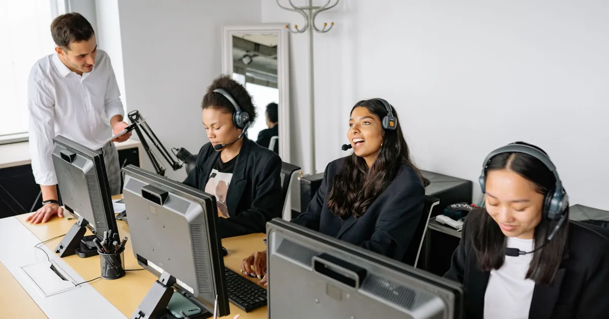 A diverse team of customer service representatives working in an office setting, wearing headsets and using computers.