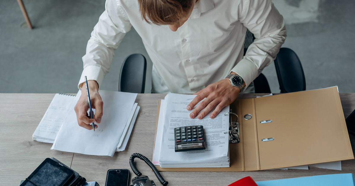Man in an office reviewing financial papers with a calculator on a desk.
