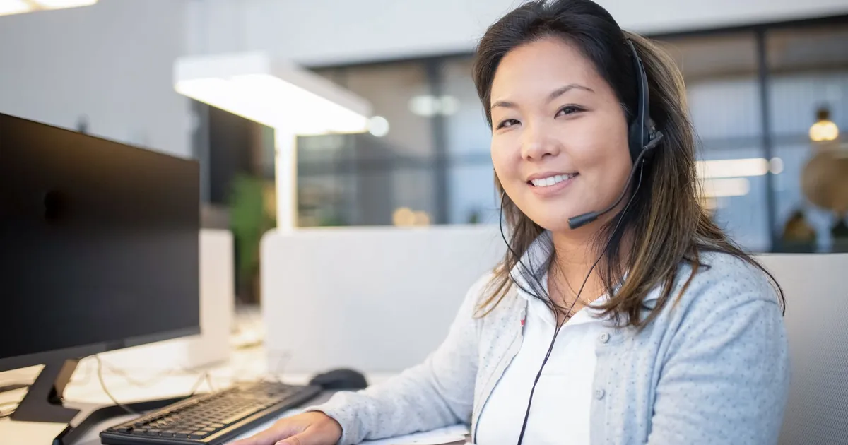 Smiling call center agent wearing a headset while working at her desk in a modern office setting.