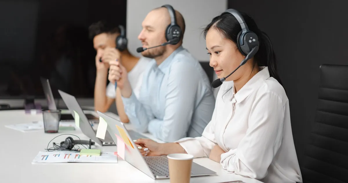 Call center agents wearing headsets working on laptops at a customer support team meeting.